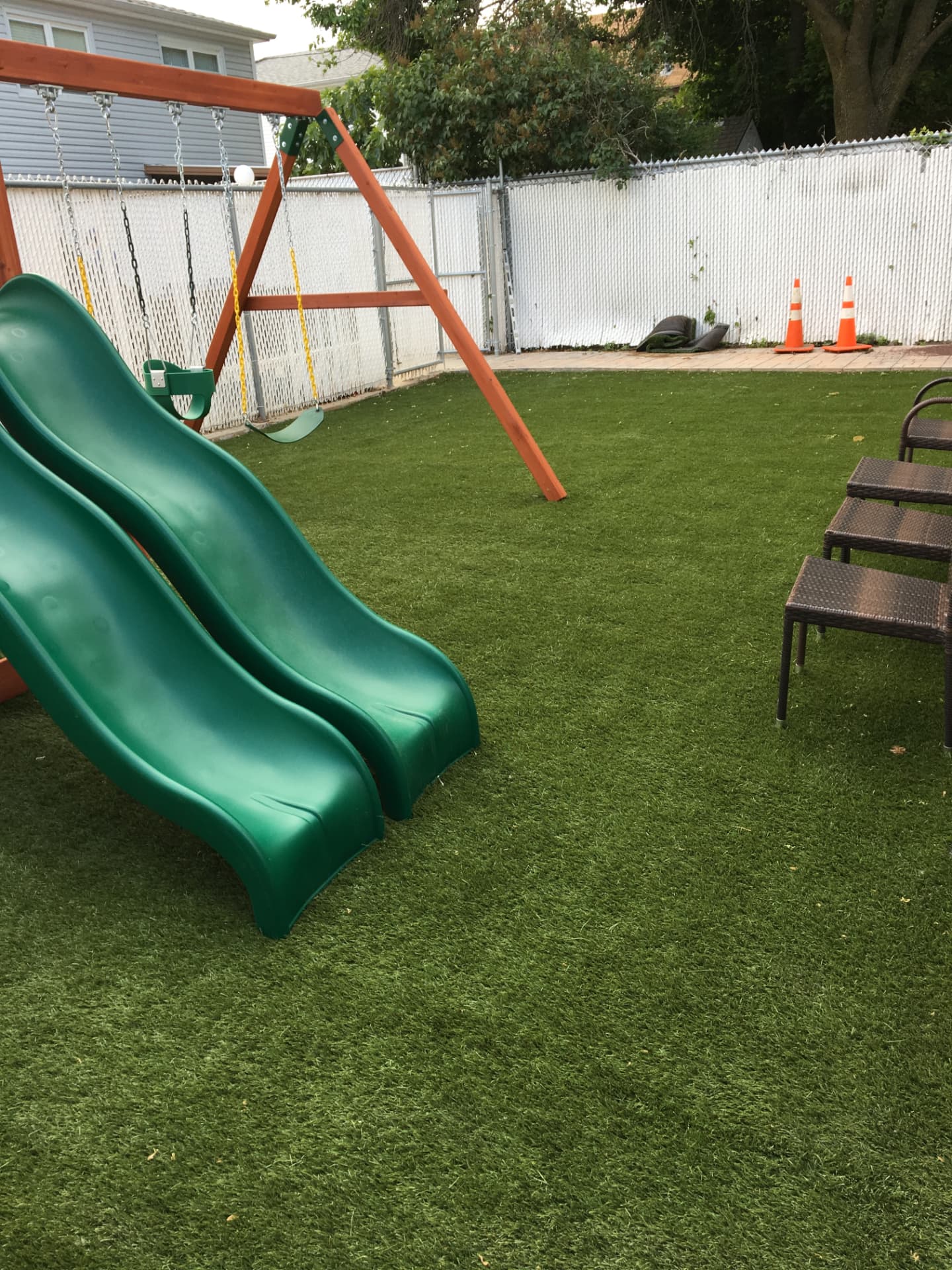 Backyard synthetic turf installation with a wooden swing set and green slides