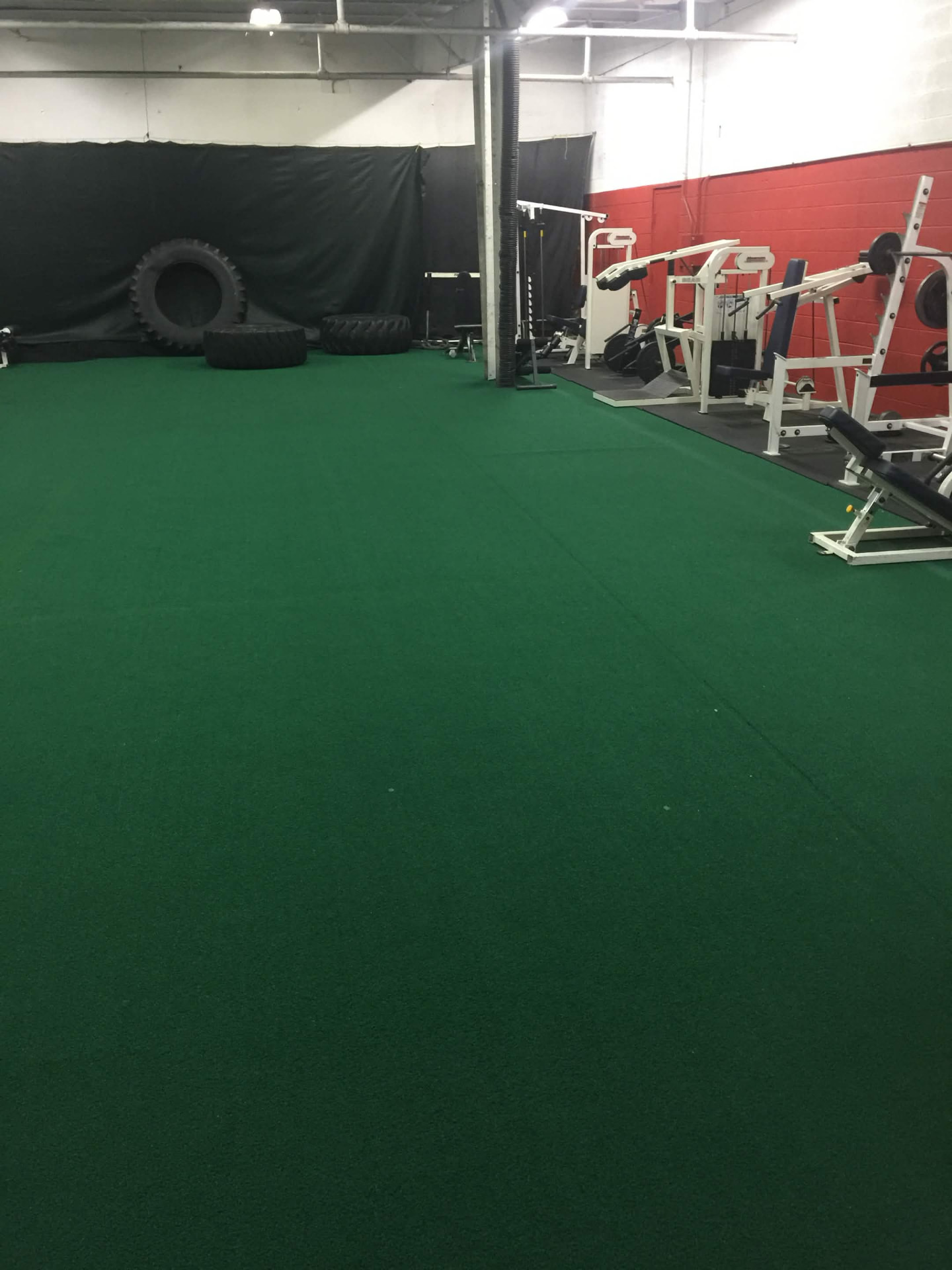 Green turf flooring installed across a gym training floor with weight racks and tires